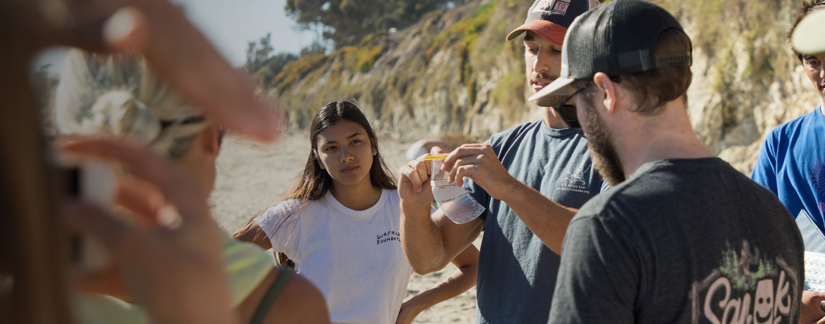 Volunteer holds up sample bag while speaking to group of volunteers standing in a circle.